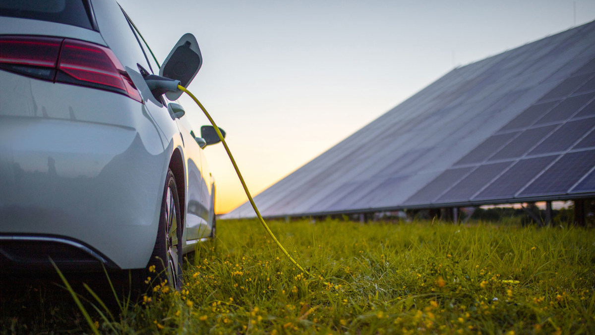 Electric car charging near solar array in clean energy landscape